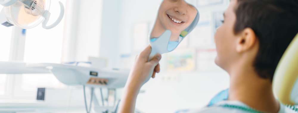 Little boy in a dental chair looking in the mirror at his teeth, pediatric dentistry, children stomatology